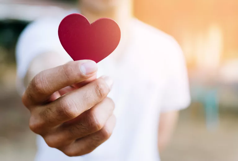 Person holding out a heart shaped piece of paper.