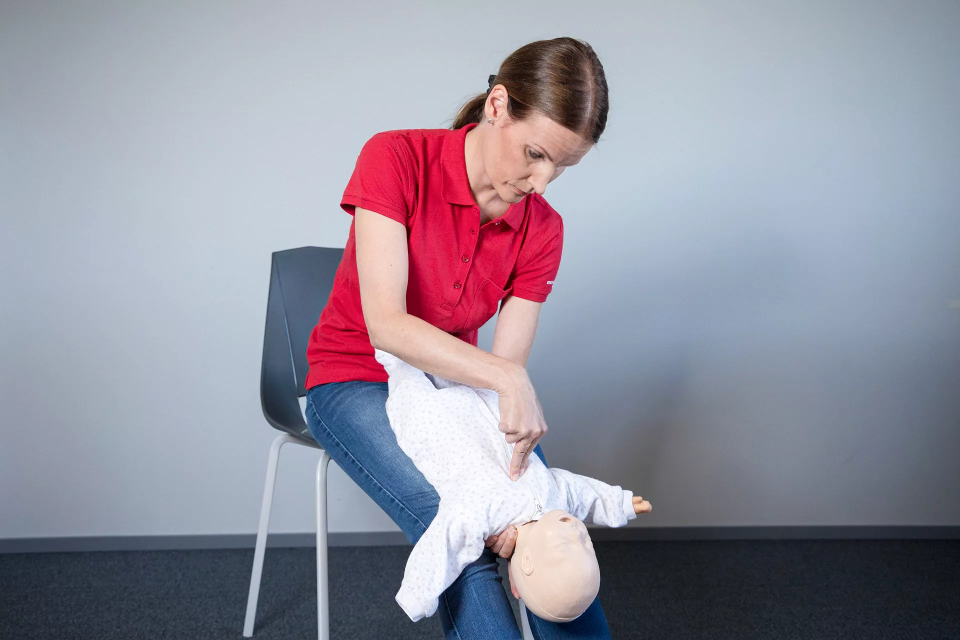 Demonstrating CPR on a baby by pressing down their sternum with two finders with the baby on their lap.