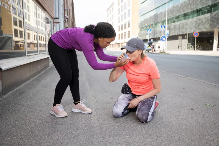 A woman helps another woman with their asthma inhalator.